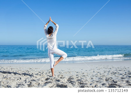 Woman practicing yoga in sportswear on sandy beach at water's edge with ocean waves and horizon Woman practicing yoga in sportswear on sandy beach at water's edge with ocean waves and horizon 135712149