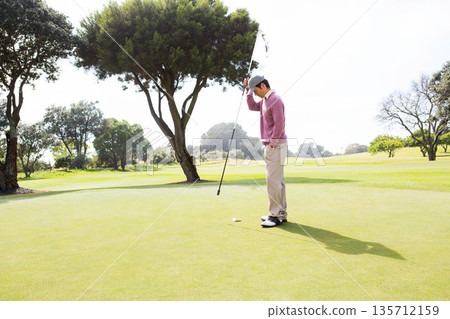 Asian man holding flagstick with white flag upright on putting green at golf course, copy space Asian man holding flagstick with white flag upright on putting green at golf course, copy space 135712159