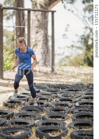 Female wearing blue athletic shirt and black leggings navigating tire obstacle course in clearing 135712173