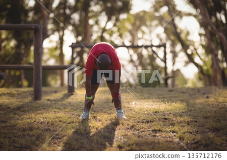 lone man bending and stretching legs wearing fitness tracker near wooden bars in grassy park 135712176