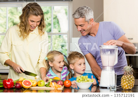 Family of four slicing fruits on cutting board and operating blender on kitchen countertop 135712191