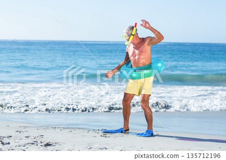 Senior man standing in shallow turquoise water at beach wearing green ring and blue fins 135712196