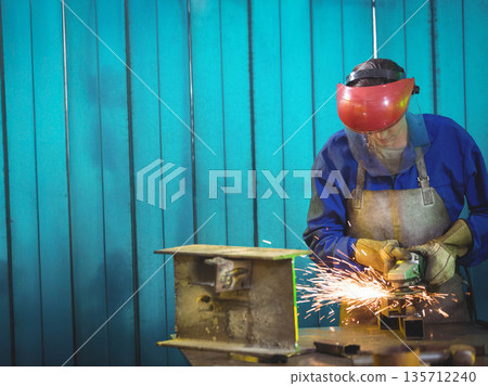 Female metalworker wearing face shield using angle grinder on shop bench with sparks, copy space 135712240