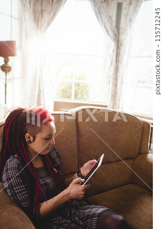 Woman with colorful dreadlocks holding tablet on beige couch in sunlit living room, copy space Woman with colorful dreadlocks holding tablet on beige couch in sunlit living room, copy space 135712245