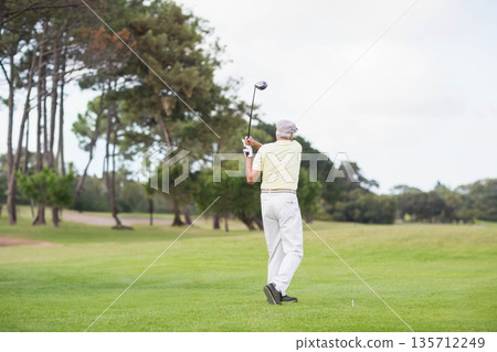 Senior man swinging golf driver on fairway at golf course wearing glove and polo, copy space Senior man swinging golf driver on fairway at golf course wearing glove and polo, copy space 135712249