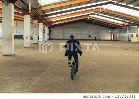 Male riding BMX bicycle inside warehouse navigating between support columns and utility boxes Male riding BMX bicycle inside warehouse navigating between support columns and utility boxes 135712311