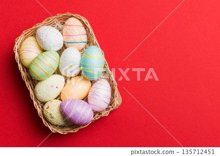 Colorful Easter eggs in wicker basket against colored background, closeup. top view with copy space Colorful Easter eggs in wicker basket against colored background, closeup. top view with copy space 135712451