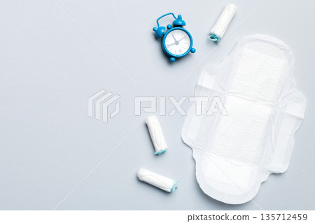 Ringing alarm clock with sanitary female tampons and menstrual sanitary pads. Medical concept of woman critical days and menstruation. Female daily hygiene. Copy space 135712459