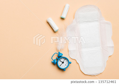 Ringing alarm clock with sanitary female tampons and menstrual sanitary pads. Medical concept of woman critical days and menstruation. Female daily hygiene. Copy space Ringing alarm clock with sanitary female tampons and menstrual sanitary pads. Medical concept of woman critical days and menstruation. Female daily hygiene. Copy space 135712461