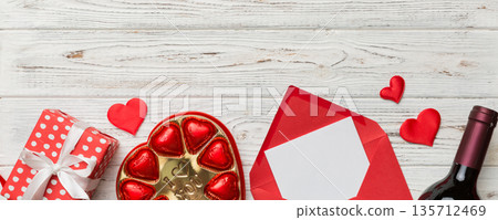 Bottle of red wine on colored background for Valentine Day with gift box, envelope and chocolate. Heart shaped with gift box of chocolates top view with copy space 135712469