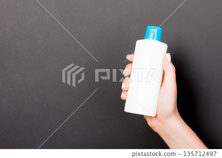 Female hand holding cream bottle of lotion isolated. Girl give tube cosmetic products on black background Female hand holding cream bottle of lotion isolated. Girl give tube cosmetic products on black background 135712497