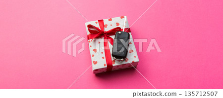 Car key on paper gift box with red ribbon bow and heart on pink table background. Holidays present top view concept Car key on paper gift box with red ribbon bow and heart on pink table background. Holidays present top view concept 135712507