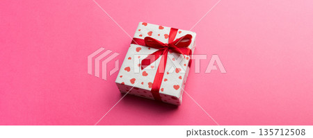 Gift box with red ribbon and heart on pink background, top view with copy space for text 135712508