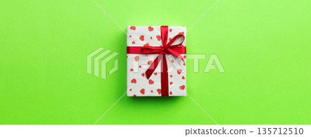 Gift box with red ribbon and heart on green background, top view with copy space for text 135712510