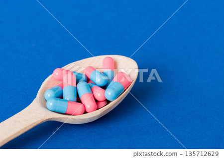 Vitamin capsules in a spoon on a colored background. Pills served as a healthy meal. Red soft gel vitamin supplement capsules on spoon Vitamin capsules in a spoon on a colored background. Pills served as a healthy meal. Red soft gel vitamin supplement capsules on spoon 135712629