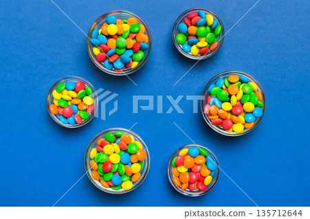 different colored round candy in bowl and jars. Top view of large variety sweets and candies with copy space different colored round candy in bowl and jars. Top view of large variety sweets and candies with copy space 135712644
