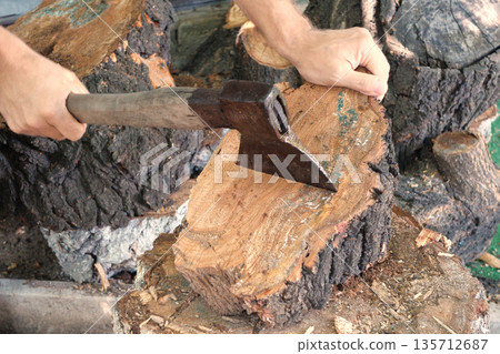 Cutting wood with a large sharp ax, Man Chops firewood, Chopping of wood on a wooden log in summer at the home 135712687