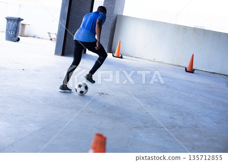 African American male athlete dribbling soccer ball past orange cones in parking garage, copy space African American male athlete dribbling soccer ball past orange cones in parking garage, copy space 135712855