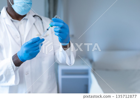 African American male doctor drawing medication from vial into syringe in clinic, copy space African American male doctor drawing medication from vial into syringe in clinic, copy space 135712877