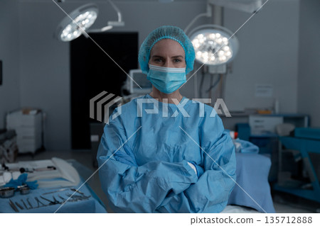 Female surgeon standing in operating room wearing blue gown organizing tools under surgical lights Female surgeon standing in operating room wearing blue gown organizing tools under surgical lights 135712888