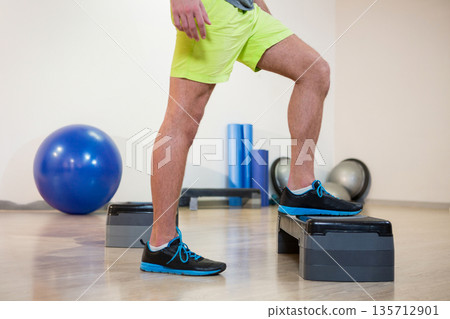 Male exerciser performing step-up exercise on platform in gym with stability ball and Bosu balls Male exerciser performing step-up exercise on platform in gym with stability ball and Bosu balls 135712901