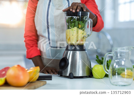 African American female operating blender with leafy greens in home kitchen with halved citrus African American female operating blender with leafy greens in home kitchen with halved citrus 135712903