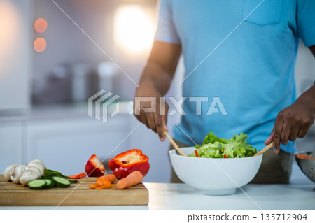 Mid adult African American man mixing salad in bowl in kitchen with wooden spoons, copy space Mid adult African American man mixing salad in bowl in kitchen with wooden spoons, copy space 135712904