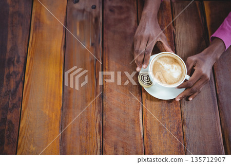 African American man wearing magenta shirt holding coffee cup and cookie on cafe table, copy space African American man wearing magenta shirt holding coffee cup and cookie on cafe table, copy space 135712907