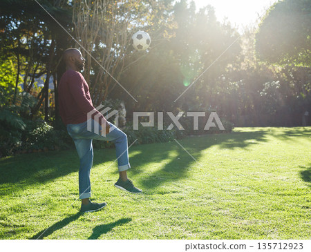 Mature African American man tapping soccer ball upward with knee in residential garden, copy space Mature African American man tapping soccer ball upward with knee in residential garden, copy space 135712923