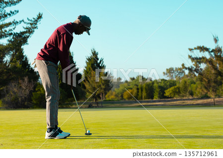 African American man lining up putt on putting green holding putter and ball, copy space 135712961