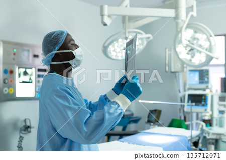 African American male adult surgeon examining X-ray film under LED lamps in hospital OR, copy space African American male adult surgeon examining X-ray film under LED lamps in hospital OR, copy space 135712971