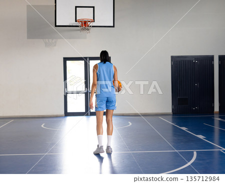 African American male athlete wearing jersey standing near hoop on court holding orange basketball 135712984
