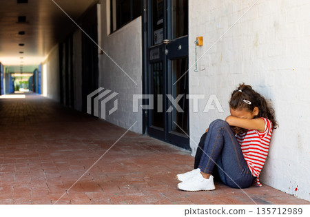 Girl child sitting on red brick corridor floor in covered hallway wearing striped shirt, copy space Girl child sitting on red brick corridor floor in covered hallway wearing striped shirt, copy space 135712989