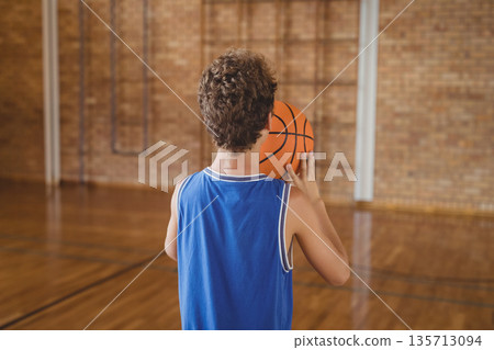 Boy dribbling basketball across polished wooden court inside school gym by brick wall with pipes Boy dribbling basketball across polished wooden court inside school gym by brick wall with pipes 135713094