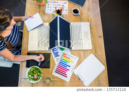 Indian woman working at office workspace while sketching on tablet with laptops, coffee, copy space 135713128