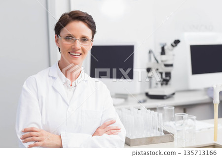 Mid adult woman scientist standing at lab bench with microscope and test tubes, copy space 135713166