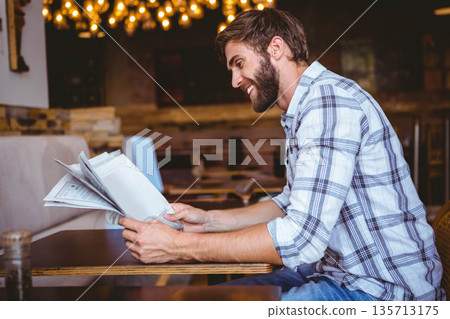 Adult man sitting at table in cozy cafe with hanging string lights reading newspaper, copy space Adult man sitting at table in cozy cafe with hanging string lights reading newspaper, copy space 135713175