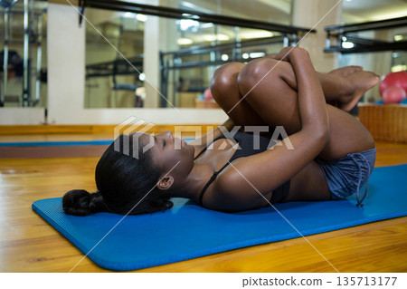 African American woman in sportswear pulling knees to chest on yoga mat in studio with balls African American woman in sportswear pulling knees to chest on yoga mat in studio with balls 135713177
