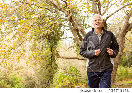 Senior man jogging park trail wearing dark running jacket, track pants, athletic shoes, copy space Senior man jogging park trail wearing dark running jacket, track pants, athletic shoes, copy space 135713188