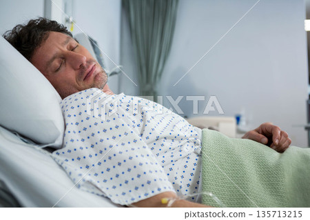 Senior male patient lying in hospital room on bed wearing patterned gown and holding IV line Senior male patient lying in hospital room on bed wearing patterned gown and holding IV line 135713215
