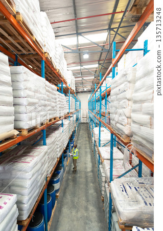 African American man wearing helmet scanning inventory in warehouse aisle with tall shelving racks African American man wearing helmet scanning inventory in warehouse aisle with tall shelving racks 135713248