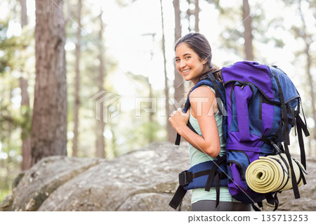 Female hiker standing on rock at pine forest trail carrying backpack and sleeping mat, copy space 135713253