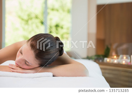 Woman receiving massage on table in spa room wearing white towel beside lit candles on shelf Woman receiving massage on table in spa room wearing white towel beside lit candles on shelf 135713285