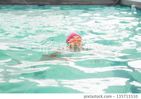 African American boy swimming with pink swim cap and orange swim goggles at pool facility 135713310