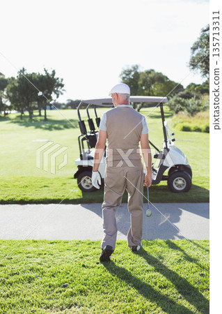 Senior male golfer walking along cart path toward parked golf cart holding club with gloved hand Senior male golfer walking along cart path toward parked golf cart holding club with gloved hand 135713311