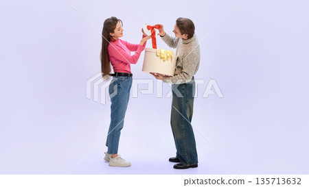 Couple opening small gift together with large box during Valentine celebration Couple opening small gift together with large box during Valentine celebration 135713632