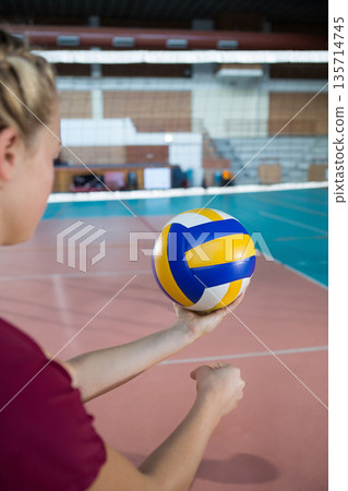 Teenage female athlete holding volleyball and preparing serve on gym court near net, copy space Teenage female athlete holding volleyball and preparing serve on gym court near net, copy space 135714745