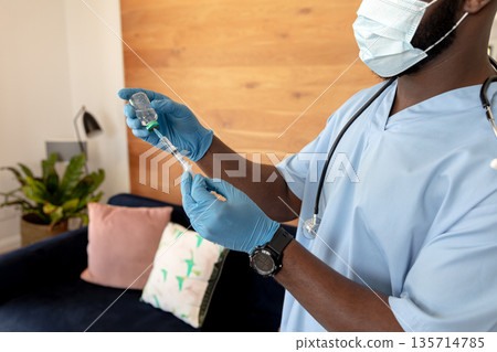 African American male wearing scrubs, stethoscope filling syringe via vaccine vial home, copy space African American male wearing scrubs, stethoscope filling syringe via vaccine vial home, copy space 135714785