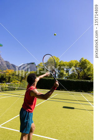 African American male athlete serving yellow tennis ball on grass court with racket and net African American male athlete serving yellow tennis ball on grass court with racket and net 135714809
