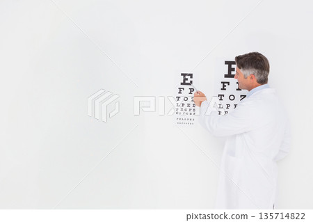Senior male optometrist pointing with pointer at Snellen eye chart in eye exam room, copy space Senior male optometrist pointing with pointer at Snellen eye chart in eye exam room, copy space 135714822